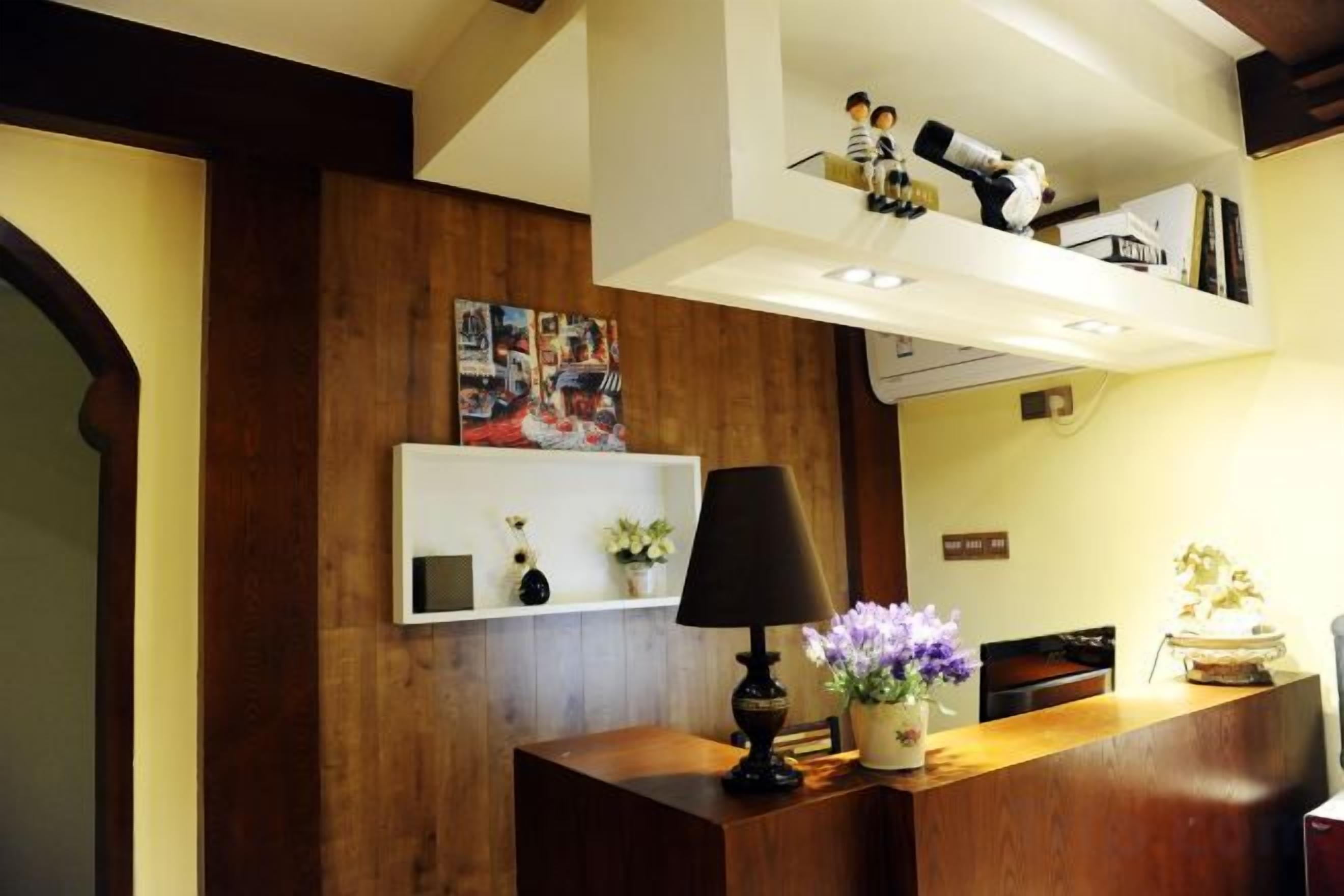 Un comptoir d’accueil avec une lampe, un vase de fleurs et une étagère ornée d’objets décoratifs.