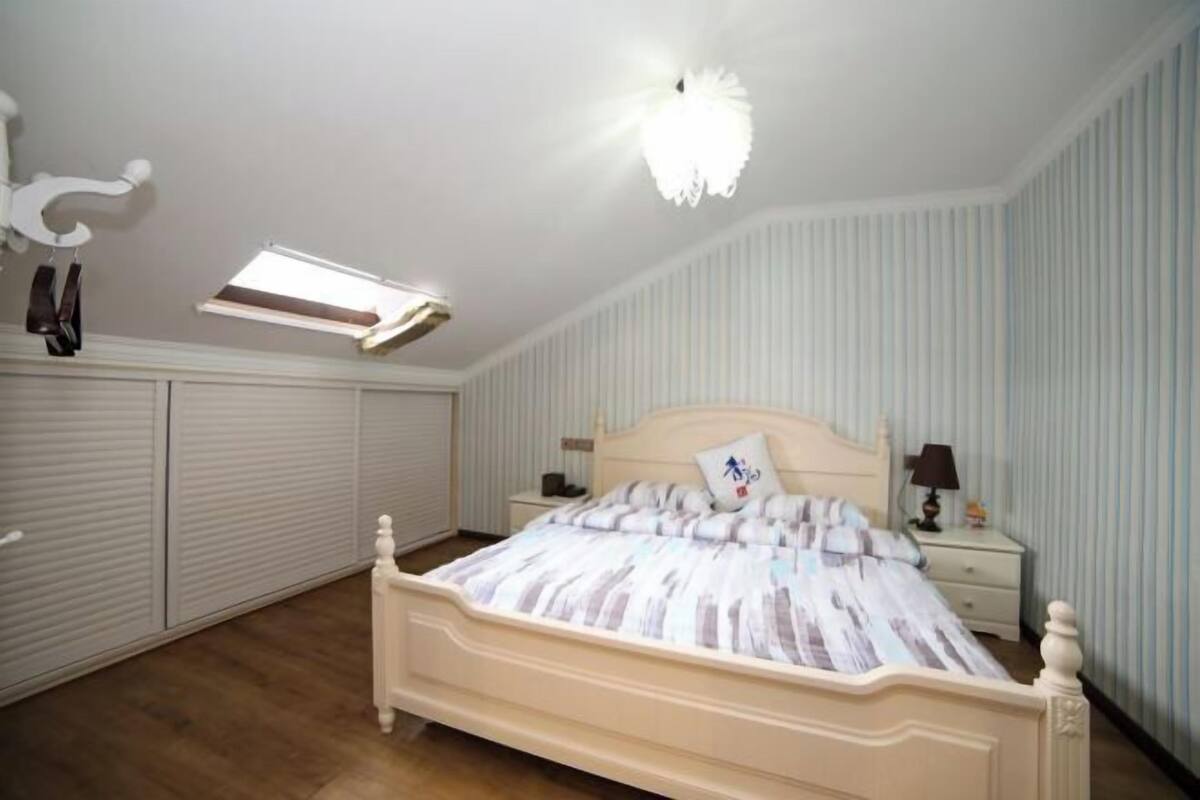 Une chambre à coucher avec un lit, des tables de chevet, une commode, un luminaire au plafond et une fenêtre.