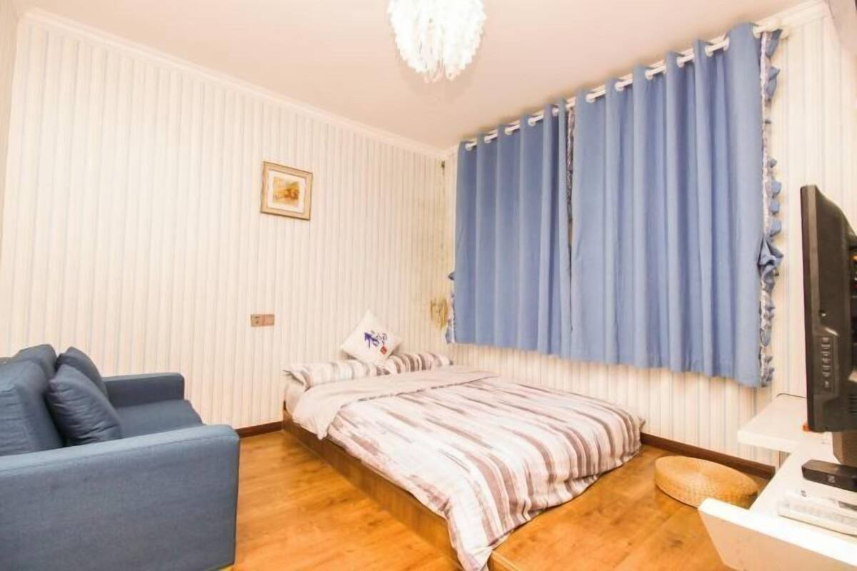 Une chambre à coucher avec un lit, un canapé bleu, une télévision et une fenêtre avec des rideaux.
