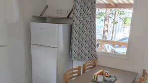 Eine kleine Küche mit Kühlschrank, einem Esstisch mit Stühlen und einem Fenster mit Blick ins Freie.