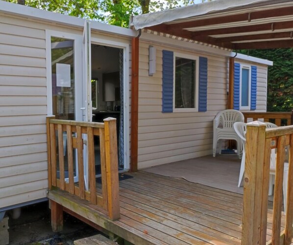 A mobile home with a wooden deck, a covered porch, and a small patio area with a chair.