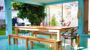 Une table en bois avec des bancs, installée dans un espace extérieur abrité dont le sol est de couleur turquoise.
