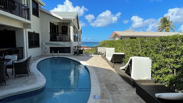Une piscine avec des chaises longues, un patio couvert et une vue sur l’océan.