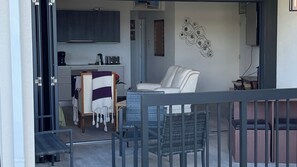 A modern kitchen with dark cabinets, a coffee machine, and a dining area with a white chair and a wicker table. - Zinnia #7 - by Zenbreak (Prospect)