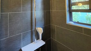 Une salle de bain avec des carreaux de couleur sombre, une pomme de douche et une fenêtre donnant sur un paysage verdoyant.