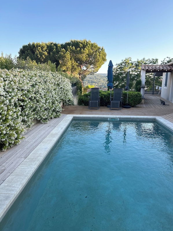 A rectangular swimming pool with a wooden deck and lounge chairs. - Maison à la Hauteur d un Beau Village (Apt)