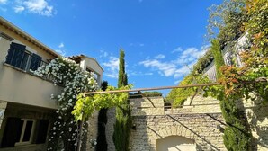 A courtyard with a stone wall, a small garden, and a pergola with white flowers. - Maison à la Hauteur d un Beau Village (Apt)