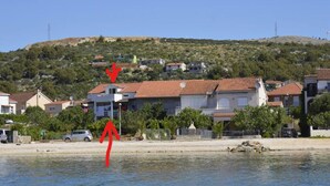 A coastal building with a red roof, surrounded by greenery and a clear sky.