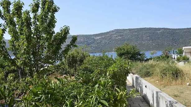 A view of a coastal area with a body of water, a hill in the background, and a building with a balcony overlooking the scene.