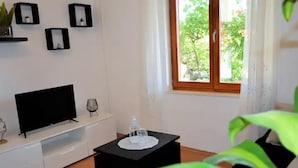 A modern living room with a flat-screen TV, a small table with a decorative item, and a window with a view of greenery.