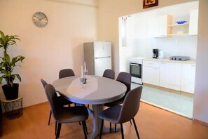 A compact living space with a dining area featuring a round table and six chairs, a small kitchen with white cabinets, a refrigerator, and a coffee maker. - Beachside Apartment - Sleeps 5, Parking & Views (Marina)