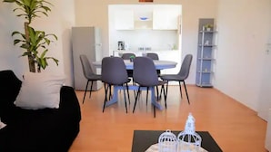 A modern living room with a black sofa, a dining table with six chairs, a small potted plant, and a decorative birdcage on a rug.