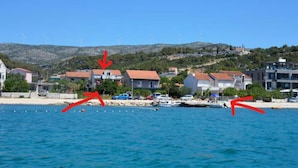 A coastal town with houses, a beach, and wind turbines in the background.