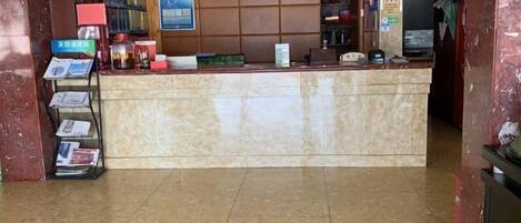A hotel reception area with a marble counter, a reception desk, and a bulletin board with information.