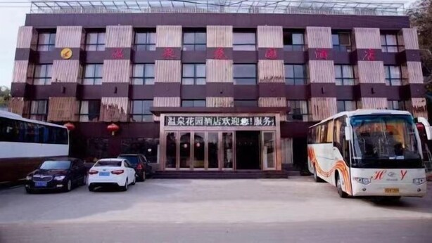 A building with a central entrance, multiple windows, and a parking area with vehicles. - Liyang Hot Spring Garden Hotel (Liyang)