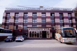 Un edificio con entrada central, varias ventanas y un estacionamiento con vehículos.
