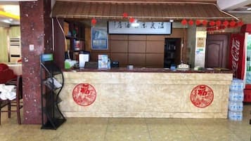 A hotel reception desk with a sign above it, a Coca-Cola refrigerator, and a red circular emblem on the wall.