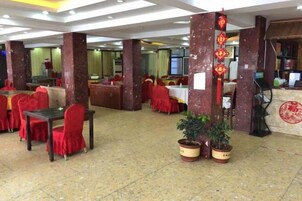 Un restaurante espacioso con sillas y mesas rojas, pilares de mármol y plantas en macetas.