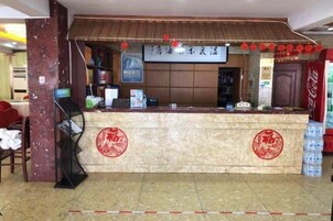 Zona de recepción de un hotel con mostrador de mármol, adornos circulares rojos, un refrigerador de Coca-Cola y un letrero con caracteres chinos.