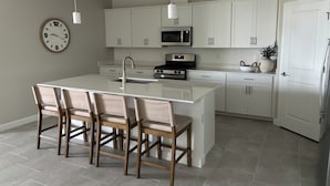 A modern kitchen with white cabinets, a central island with bar stools, a microwave, and a clock on the wall.