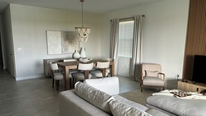 A modern living room with a sofa, dining table, chairs, and a television.