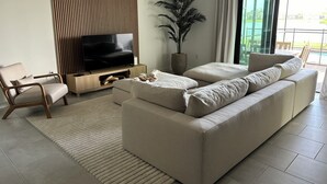 A modern living room with a sofa, a TV, a wooden panel wall, a plant, and a view of the outdoors.