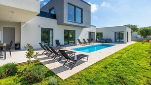 Una casa moderna de dos pisos con piscina, mobiliario exterior y césped bien cuidado.