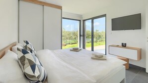Un dormitorio moderno con una cama grande, un televisor montado en la pared y un ventanal corredero que da a un jardín.