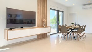 Una cocina moderna con una televisión grande, paneles de madera y un comedor con mesa dispuesta para cuatro.