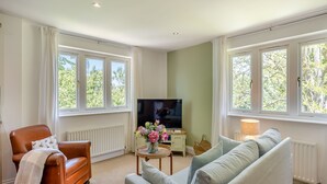 A living room with a brown leather sofa, a grey sofa, a TV, and a small table with a vase of flowers. - 1 bedroom accommodation in Wykenham, near Spalding (Wykenham, near Spalding)
