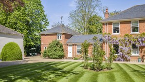 A well-maintained garden with a neatly trimmed lawn, a brick house with a white door, and a variety of trees and shrubs. - 1 bedroom accommodation in Wykenham, near Spalding (Wykenham, near Spalding)