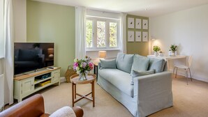 A living room with a sofa, a television, a small table with a vase, and a window with curtains. - 1 bedroom accommodation in Wykenham, near Spalding (Wykenham, near Spalding)