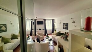 Un salon moderne avec une cloison en verre, des canapés blancs, un téléviseur à écran plat et un vase rouge.