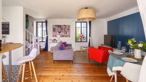 Una sala moderna con un sofá gris, sillas rojas, una mesa de comedor dispuesta con platos y vasos, y un gran ventanal con cortinas.