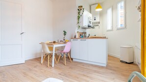 A modern kitchen with white cabinets, a wooden countertop, and a dining area with a table and chairs. - L'Atypique - Appt à 150m de la plage (Arcachon)