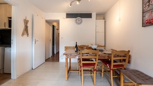 A dining area with a wooden table, chairs, and a bench. There is a clock on the wall and a bottle of wine on the table. - Le Corbier - Studio avec belle vue montagne (Villarembert)