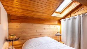 Un dormitorio con techo de madera, tragaluz, cama con ropa de cama blanca y dos lámparas de noche.