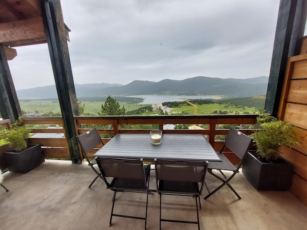 A balcony with a table and chairs, overlooking a scenic landscape with mountains and a lake. - Cosy Wood - Appt vue lac et montagne (Les Angles)