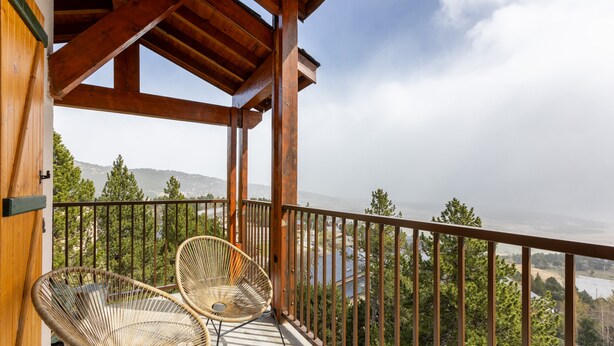 Un balcón con dos sillas de mimbre, vigas de madera y vistas a un paisaje montañoso.