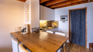 Una cocina compacta con vigas de madera, armarios blancos, cafetera y microondas.
