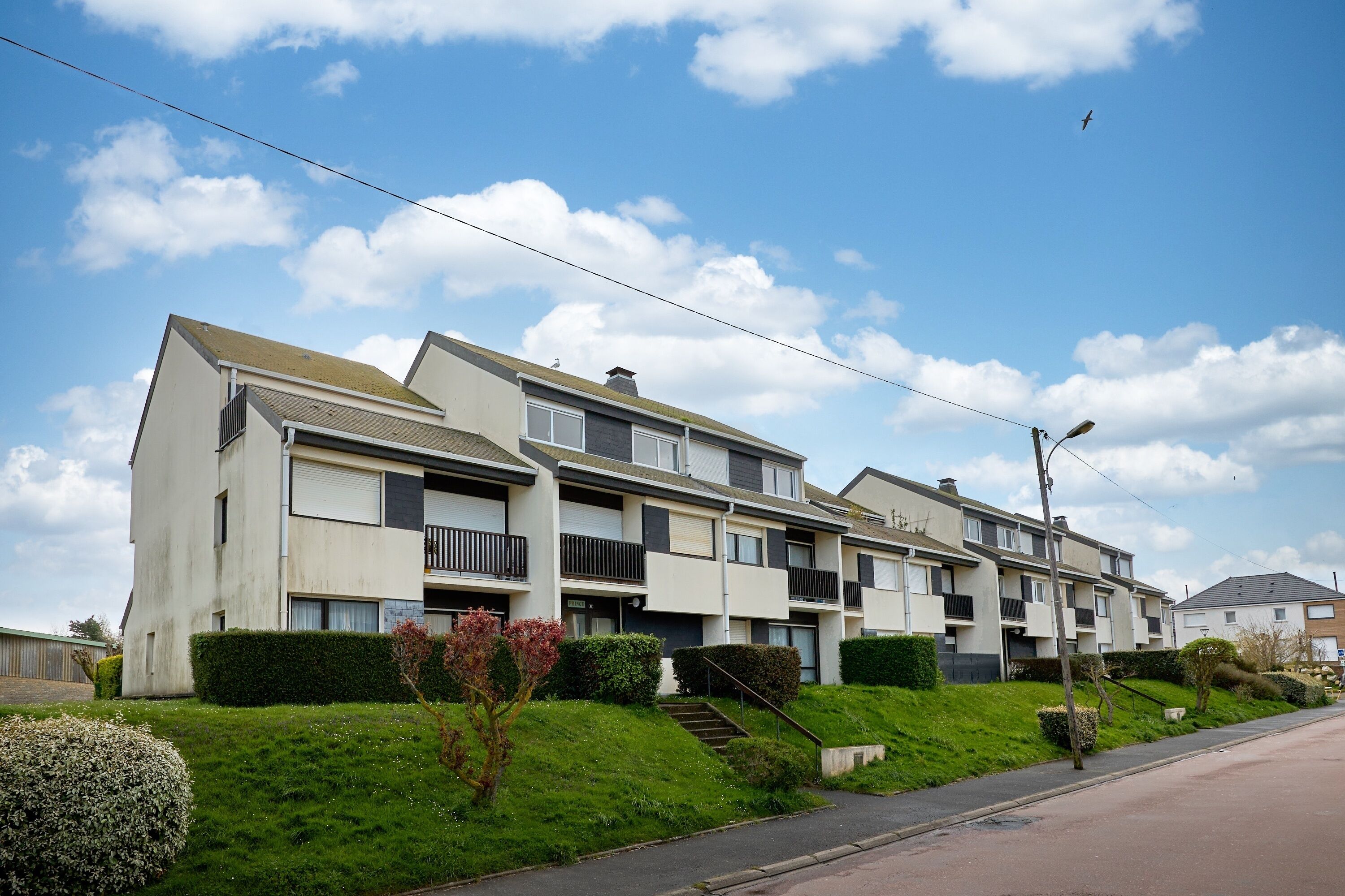 Fila de modernos edificios de apartamentos de dos pisos con balcones, cielo despejado y césped cuidado.