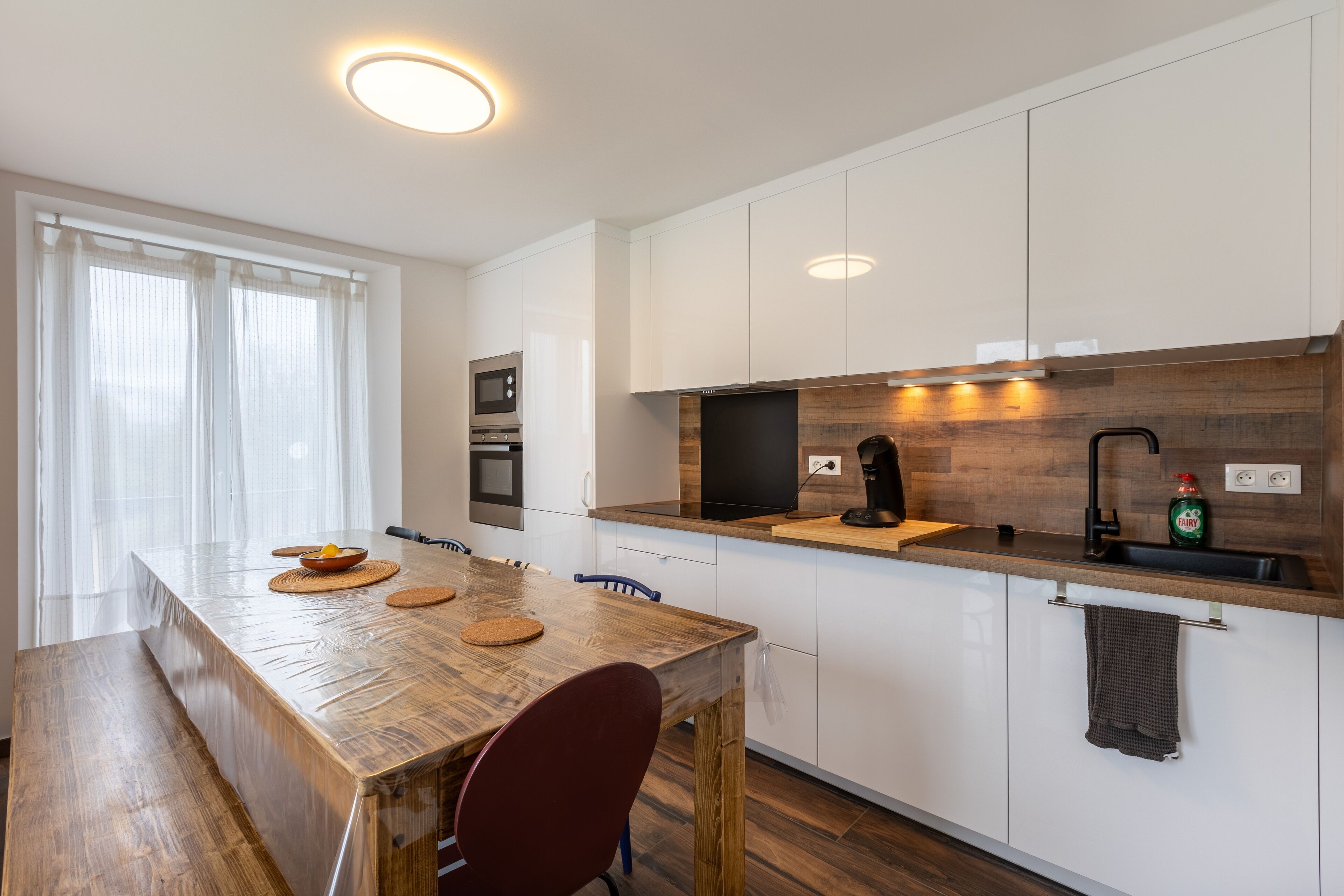 Une cuisine moderne avec des meubles blancs, un plan de travail en bois et un four encastré.