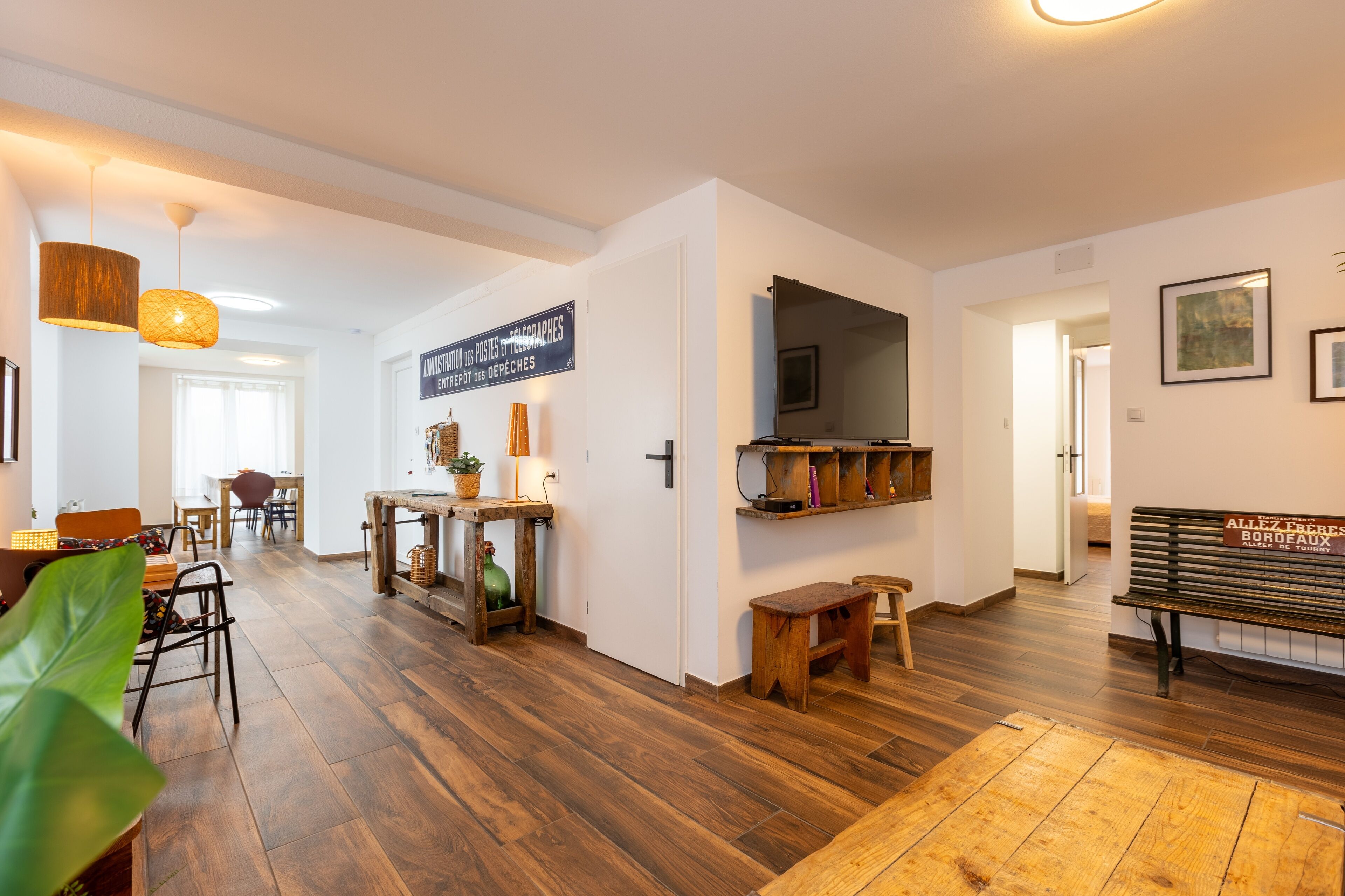 Un vaste espace de vie doté d’un plancher en bois, d’une table à manger avec des chaises, d’un banc et d’un téléviseur fixé au mur.
