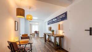 A hallway with wooden flooring, a dining table with chairs, a hanging light fixture, and a wall-mounted sign. - Cal Bourquets - Vue montagne (Err)