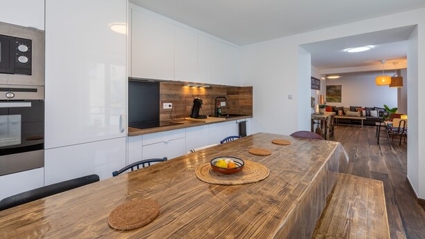 A modern kitchen with white cabinetry, a wooden countertop, and a dining area with a wooden table and chairs. - Cal Bourquets - Vue montagne (Err)