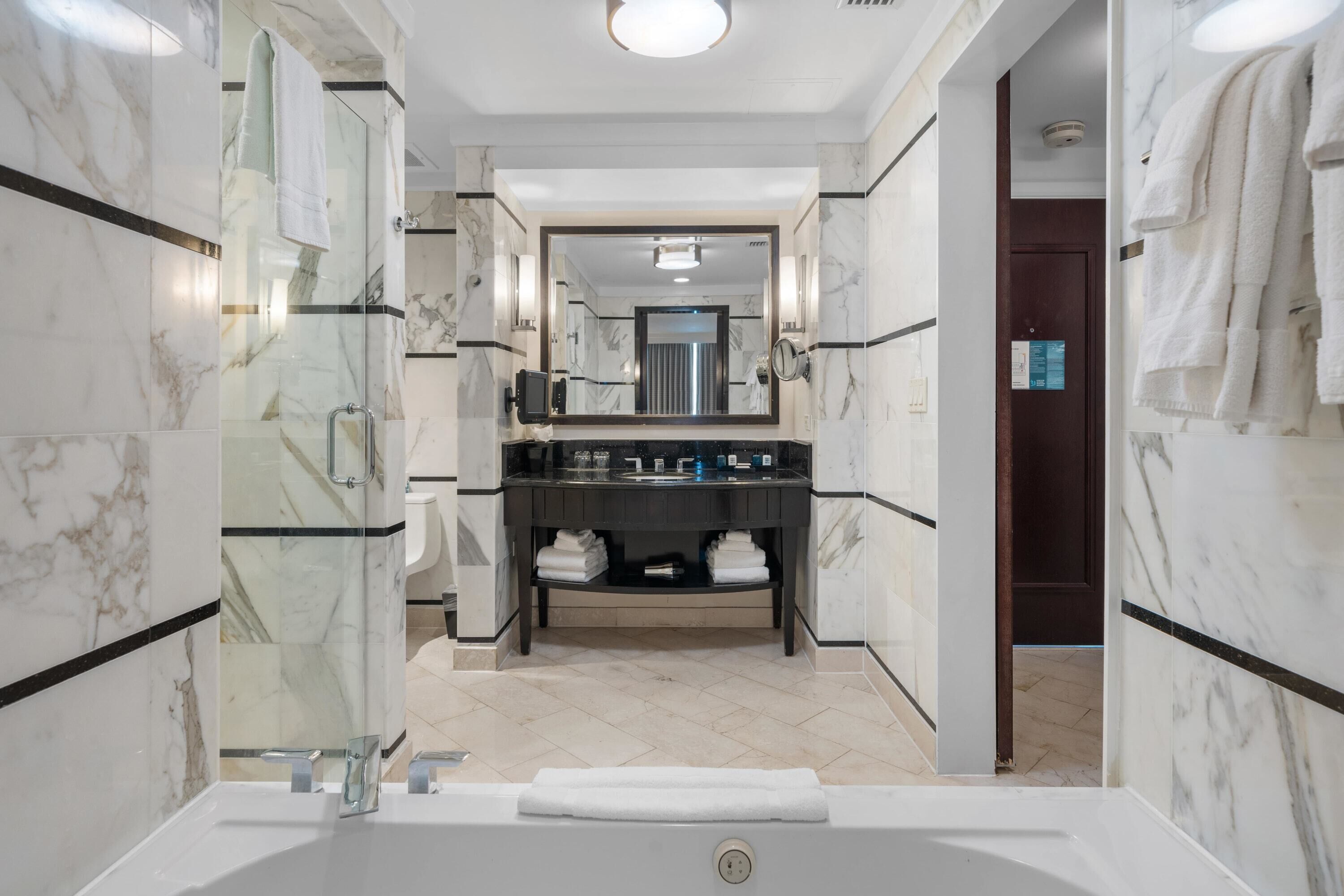 A modern bathroom with a glass-enclosed shower, a large mirror, a black vanity, and a white bathtub.