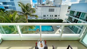 A balcony with a view of a swimming pool, palm trees, and modern buildings. - FontaineBleau Balcony 10 min from SoBe (Miami Beach)