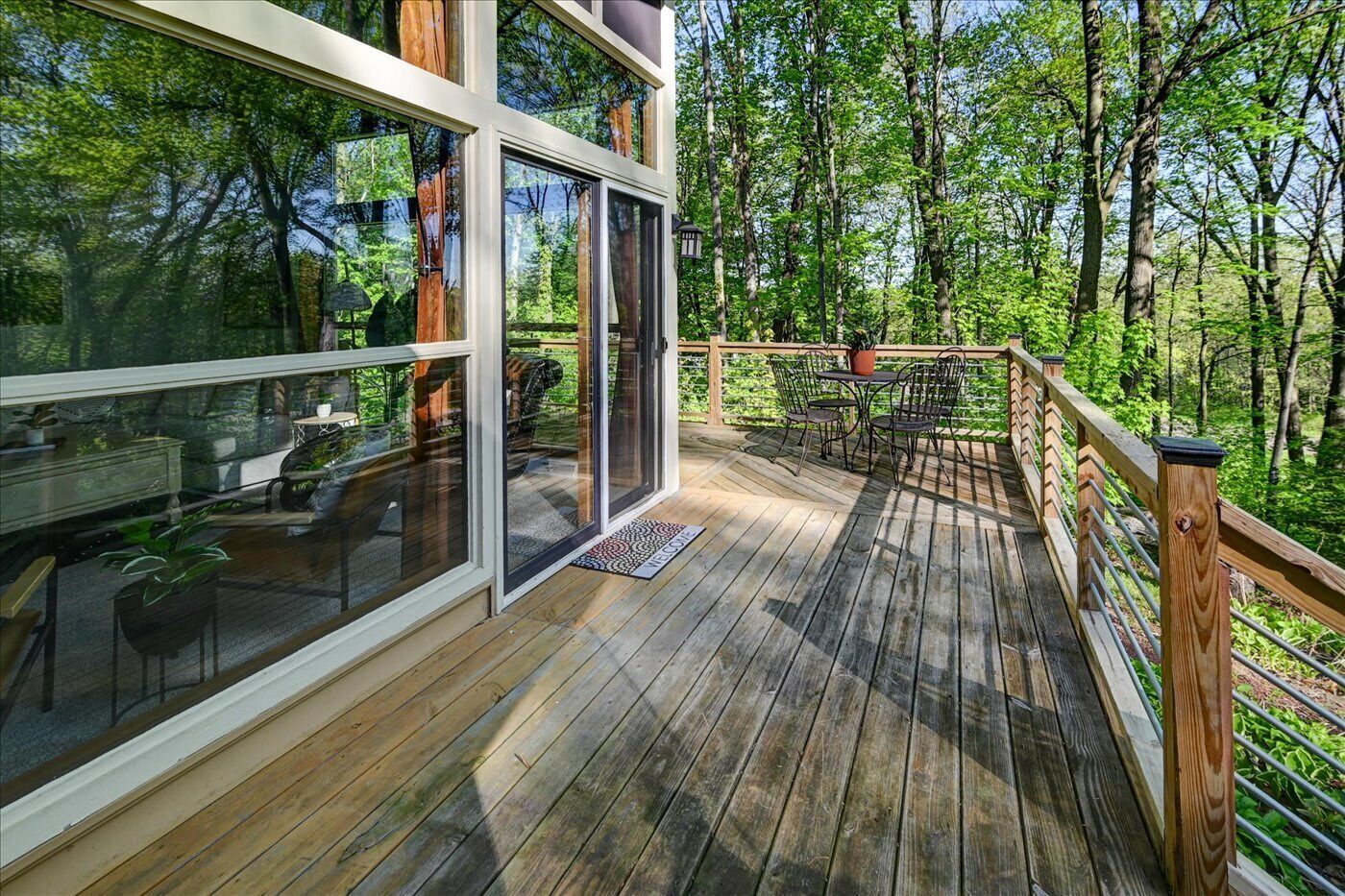 Una terraza de madera con puertas de vidrio que dan a una habitación, rodeada por un bosque.