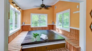 A room with a wooden bench seating area, a massage table, and large windows offering a view of the outdoors.