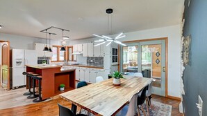 A modern kitchen with a central island, bar stools, and a dining area with a wooden table and chairs.